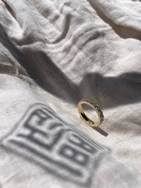 Ein goldener Ring mit Diamanten liegt auf einer strukturierten, weißen Stoffserviette in der Sonne.